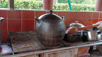A rustic kitchen with a brick stove, a large pot, and various cooking utensils.