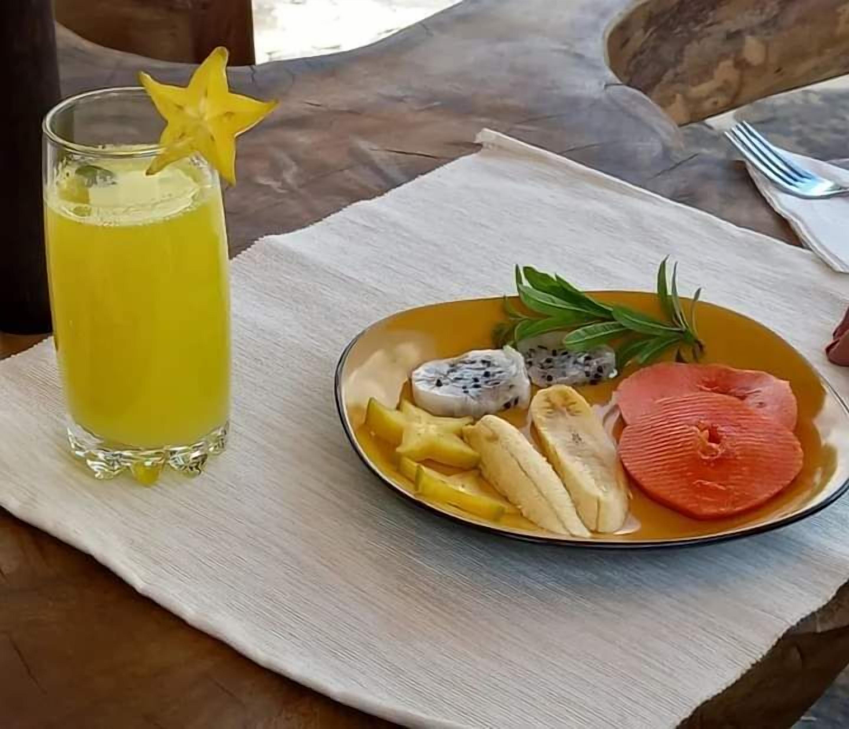 A table with a glass of yellow drink, a plate with fruits and a star-shaped garnish.