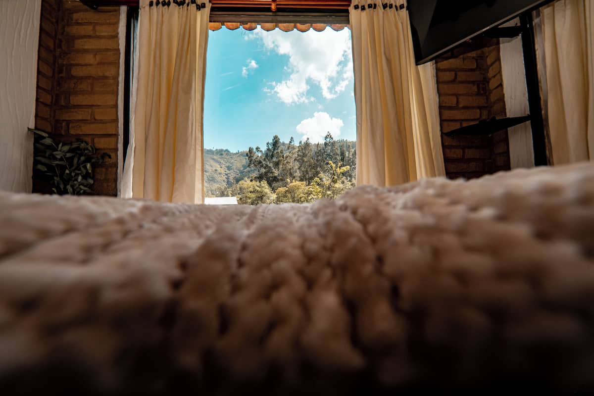 A view through a window with curtains, a brick wall, and a mountainous landscape.
