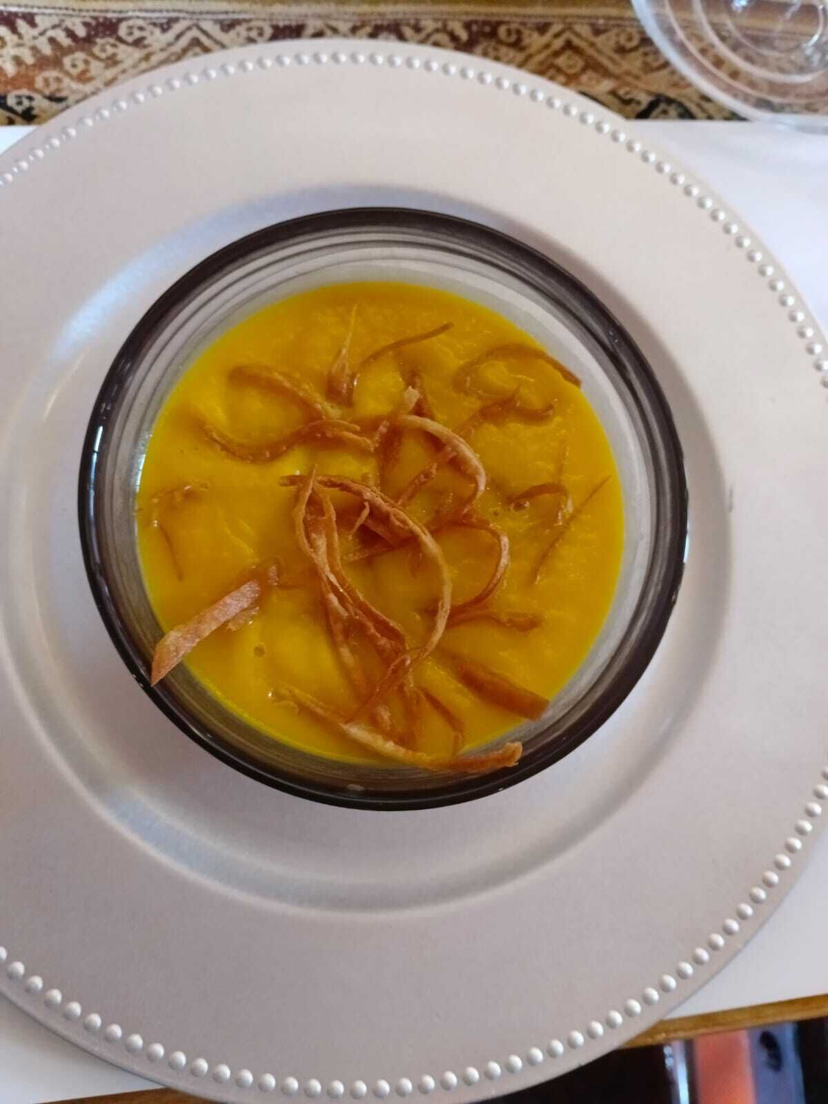 A bowl of soup with a clear broth and garnished with crispy strips, served on a white plate with a decorative edge.