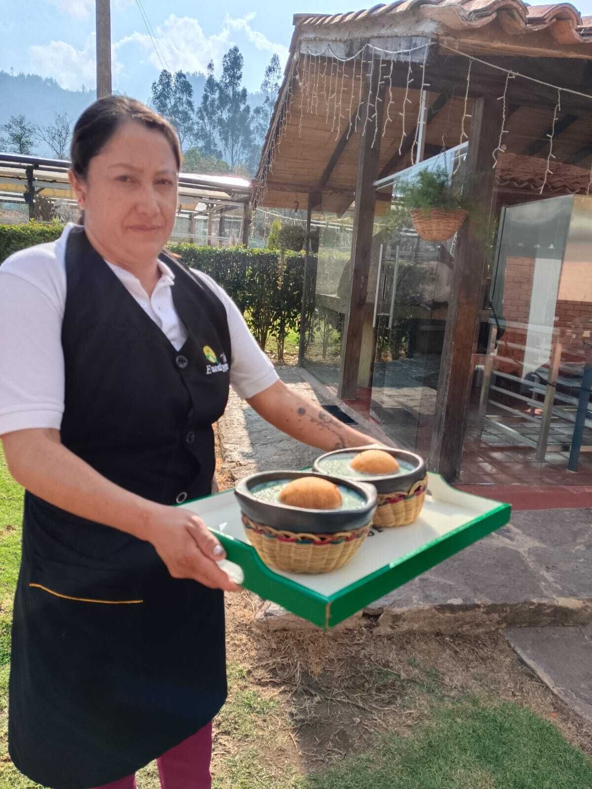 A person holding a tray with two bowls containing bread and a liquid.