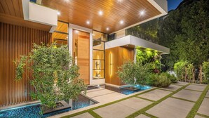 A modern house with a wooden exterior, a glass door, and a landscaped garden with a water feature.