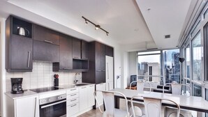 A modern kitchen with dark cabinets, white countertops, and a dining area with white chairs. - Studio 2BR Apt with GYM, Close to CN Tower (Toronto)