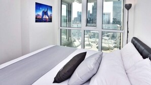 A modern hotel room with a large bed, a city view through floor-to-ceiling windows, and a painting on the wall. - Studio 2BR Apt with GYM, Close to CN Tower (Toronto)