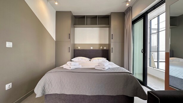 Ein modernes Schlafzimmer mit einem großen Bett, einem eingebauten Kleiderschrank und einer Schiebeglastür zum Balkon.