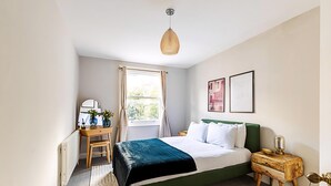 A bedroom with a bed, bedside table, lamp, and a window with curtains. - Lovely Bishops Park Flat (London)