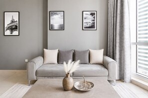 A modern living room with a grey sofa, three framed pictures on the wall, a vase with pampas grass, and a leaf-patterned bowl on the floor.