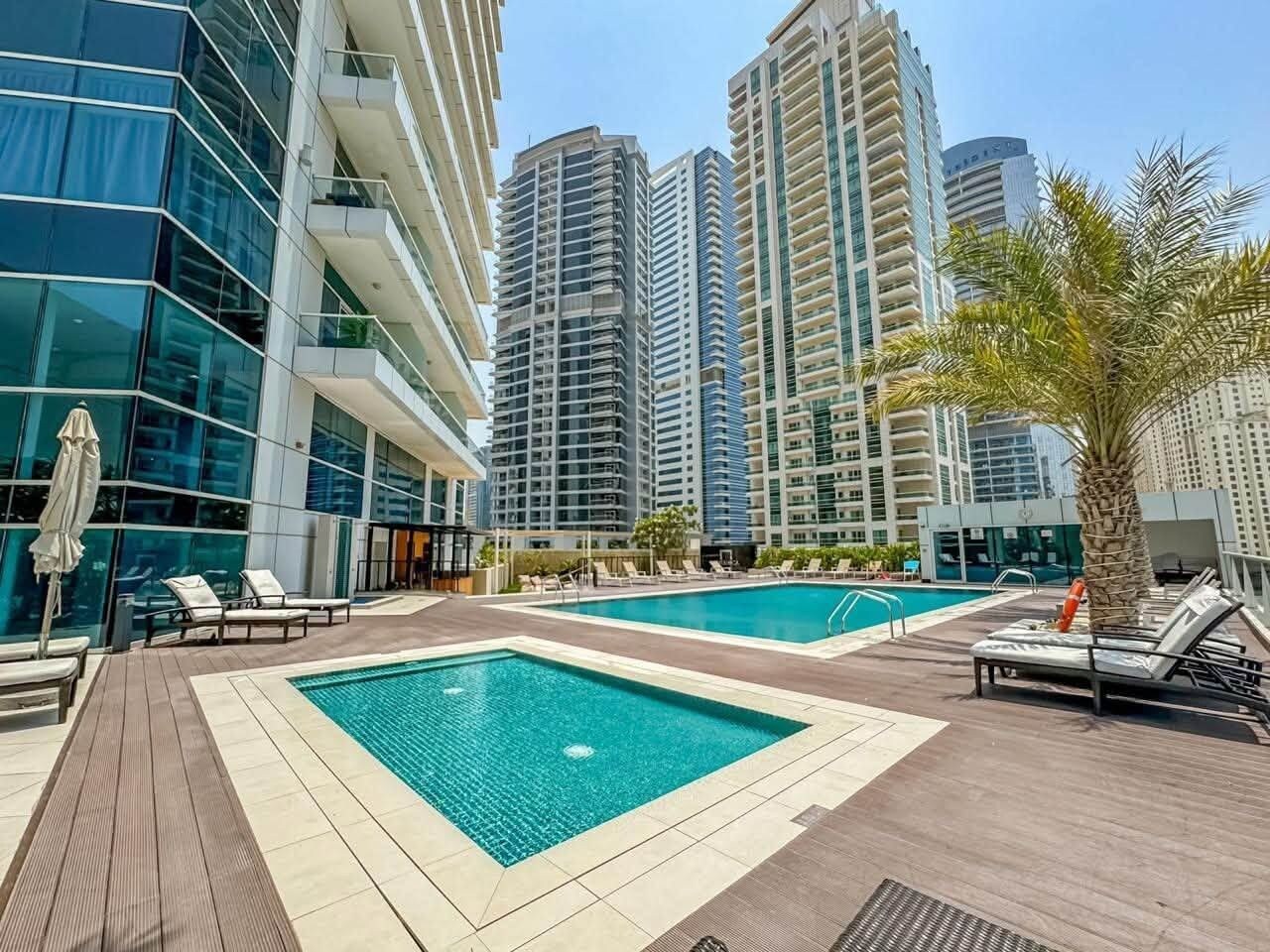 A rooftop pool area with multiple swimming pools, lounge chairs, and a palm tree.