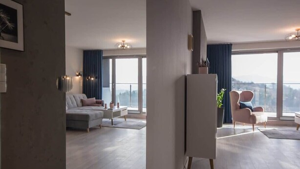 Ein modernes Wohnzimmer mit einer Couch, einem Sessel, einem Esstisch und einem großen Fenster mit Blick.