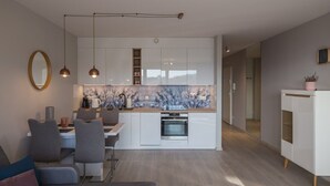 Eine moderne Küche mit weißen Schränken, einem eingebauten Ofen, Pendelleuchten und einem Essbereich mit Tisch und Stühlen.