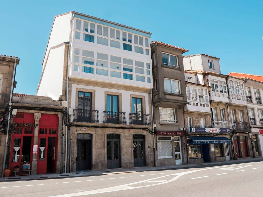 Una veduta di strada con una fila di edifici, tra cui un palazzo bianco con ampie vetrate e un negozio con vetrina rossa.