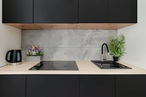 A modern kitchen with a black countertop, a black kettle, a sink, and a potted plant.