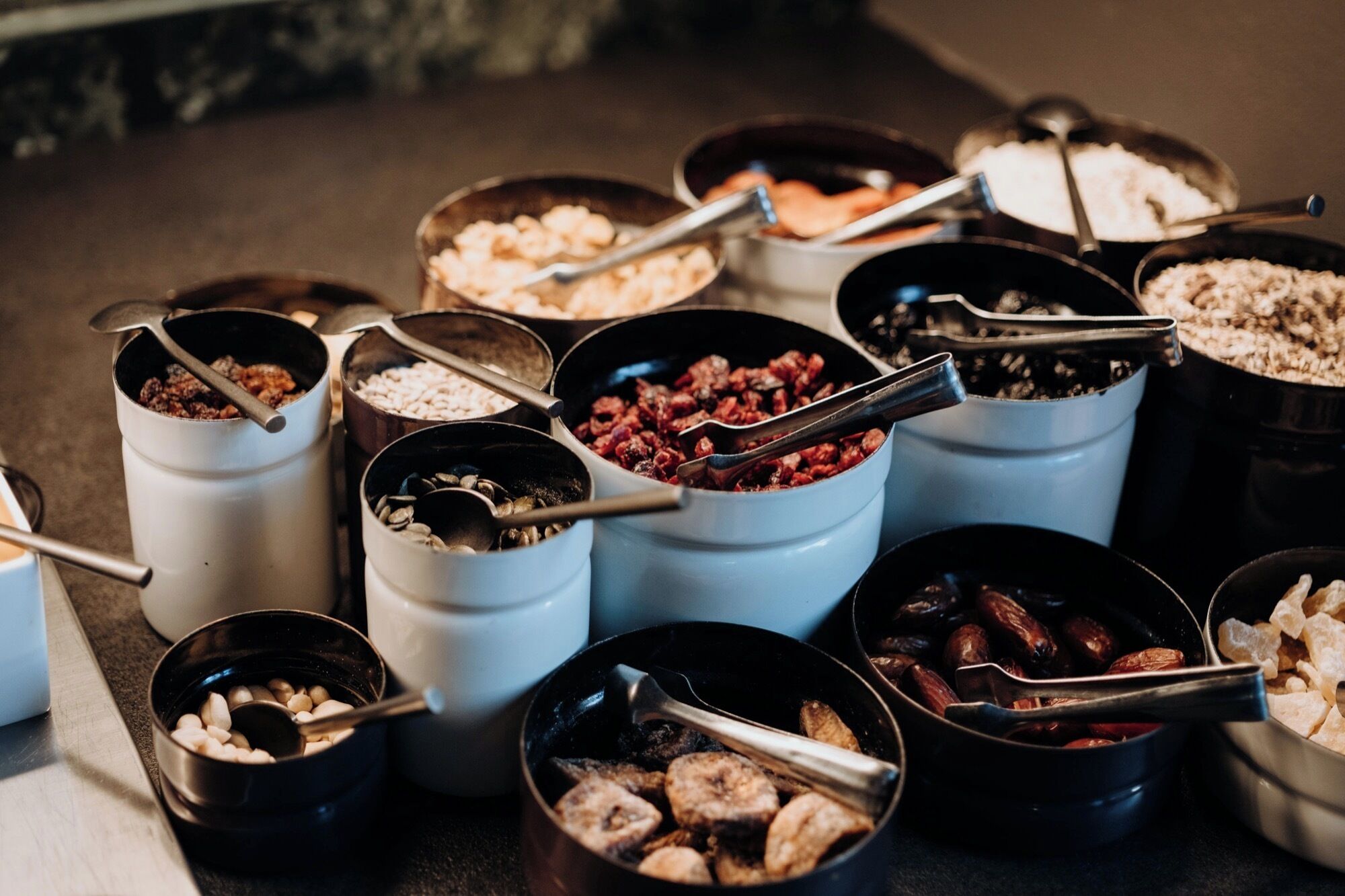 Diversi cibi esposti in contenitori, alcuni con pinze, tipico di un buffet o di un servizio di catering.