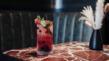 Ein hoher Schluck mit einem roten Getränk, verziert mit Beeren und Minzblättern, auf einem Marmortisch vor dunklem Hintergrund.