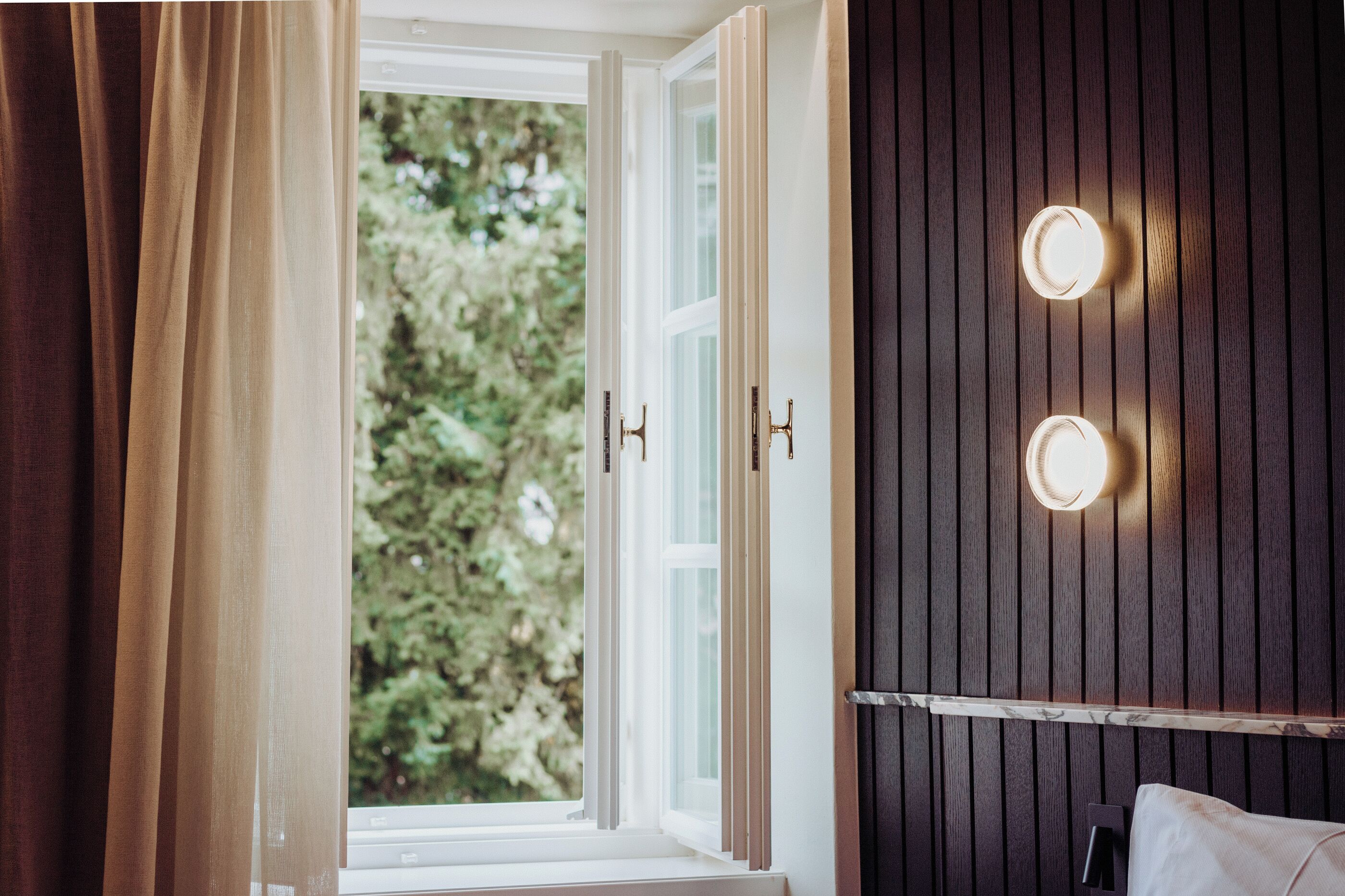 A room with a large window, wooden panel wall, and two wall-mounted lights.