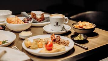 A breakfast setting with croissants, a coffee cup labeled 'Hausbrandt', and various dishes on a wooden table.
