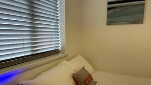 Quarto com cama, travesseiro com a inscrição 'COS' e um quadro na parede.