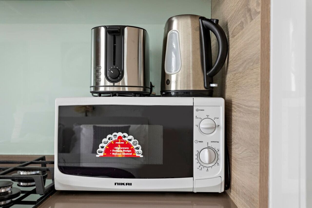 A microwave oven with a kettle and a coffee maker on top.