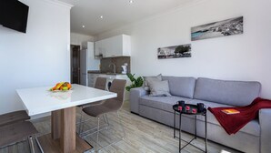 A modern living room with a grey sofa, a white dining table, and a kitchen in the background. - Pateo Loft Albufeira (Albufeira)