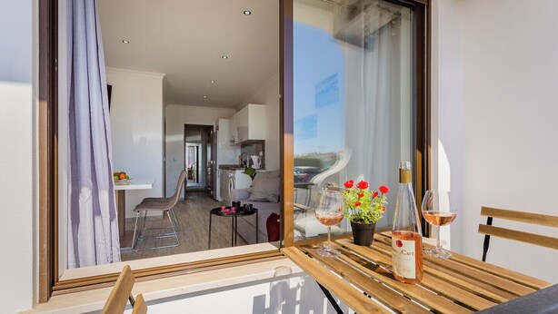 A balcony with a wooden table, two wine glasses, a bottle of wine, and a potted plant with red flowers. - Pateo Loft Albufeira (Albufeira)