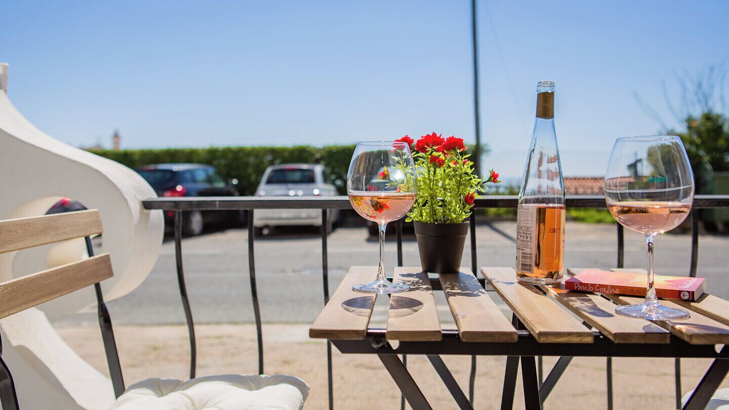 A table with two wine glasses, a bottle, and a book on a wooden bench.
