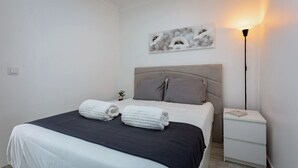 A neatly made bed with two rolled towels, a bedside lamp, and a small plant on the nightstand. - Pateo Loft Albufeira (Albufeira)