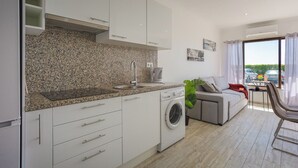 A modern kitchen with granite countertops, a built-in washing machine, and a grey sofa in a bright living area with a view of parked cars outside. - Pateo Loft Albufeira (Albufeira)