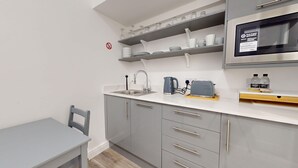 Eine moderne Küche mit grauen Schränken, einer weißen Arbeitsplatte, einer eingebauten Mikrowelle und einem Wasserkocher.