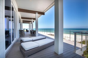 Een modern terras buiten met rieten loungesteilen en een tafel, met uitzicht op een strand.