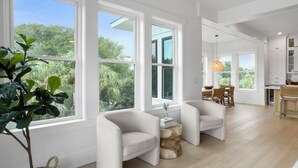 A spacious living room with large windows, a dining area, and a kitchen. - 5 BR Luxury Beach Rental w Pool, Amenities Galore (Isle of Palms)