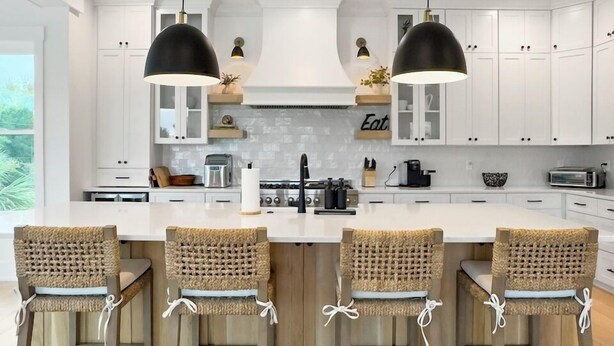A modern kitchen with white cabinetry, a central island with bar stools, pendant lighting, and a view of the outdoors. - 5 BR Luxury Beach Rental w Pool, Amenities Galore (Isle of Palms)