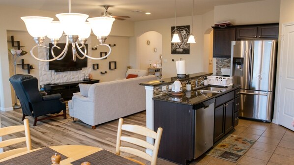 A modern kitchen with a stainless steel refrigerator, a built-in island with a sink, and a dining area with a table and chairs.