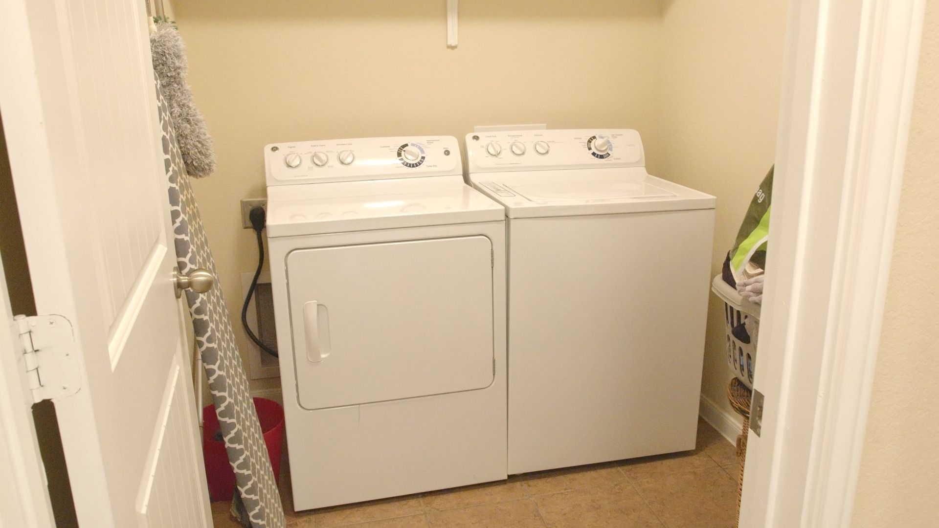 Une buanderie équipée de deux machines à laver et deux sèche-linge superposés, une porte avec un porte-serviettes et un panier à linge.