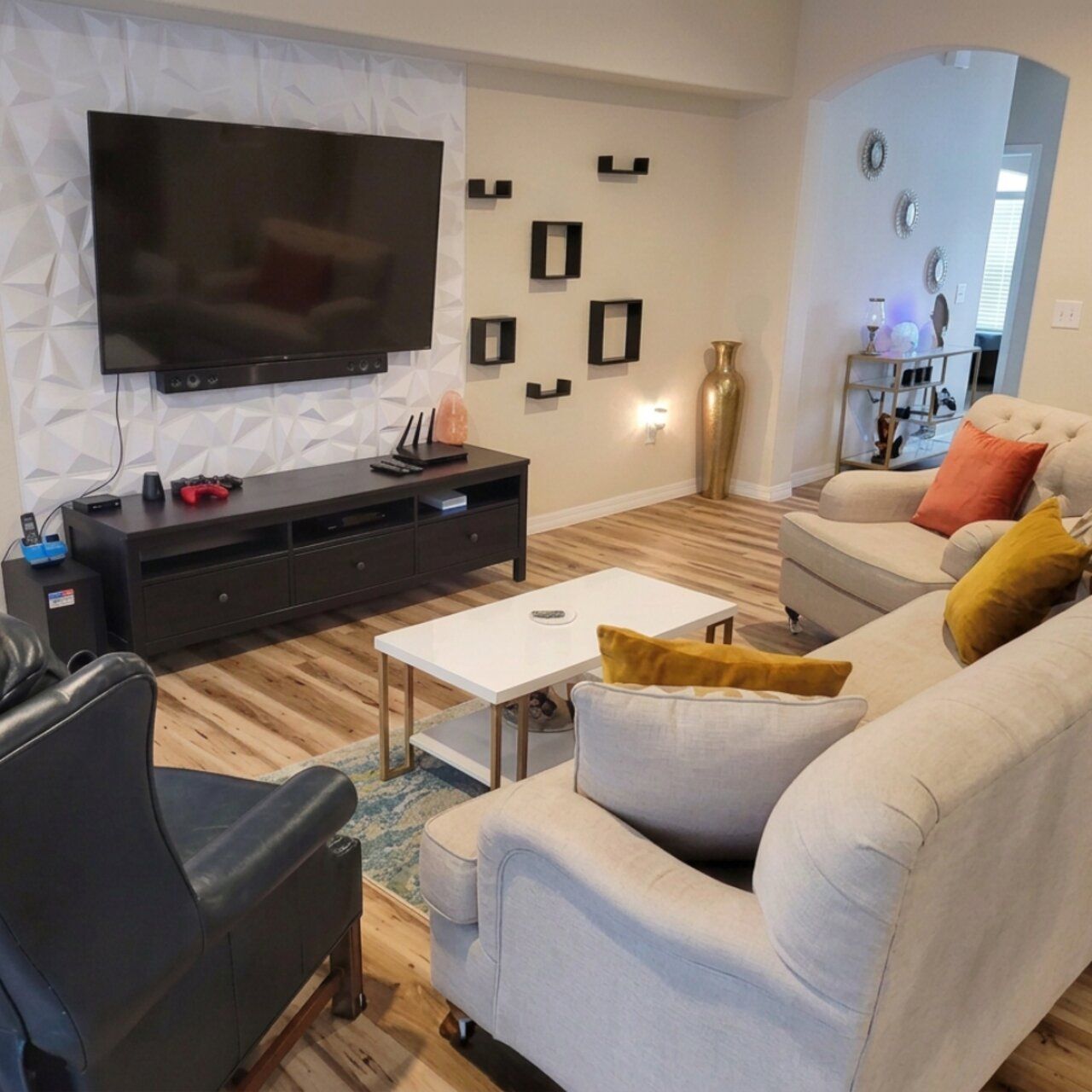 A modern living room with a flat-screen TV mounted on a textured wall, a dark entertainment unit, a light-colored sofa with cushions, and a coffee table.