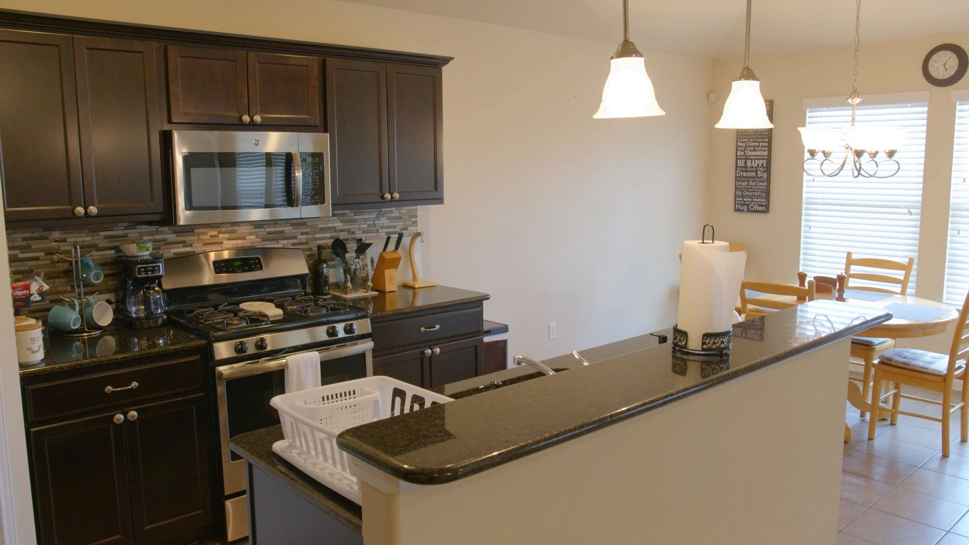 A kitchen with dark wood cabinets, stainless steel appliances, a central island, and pendant lighting.