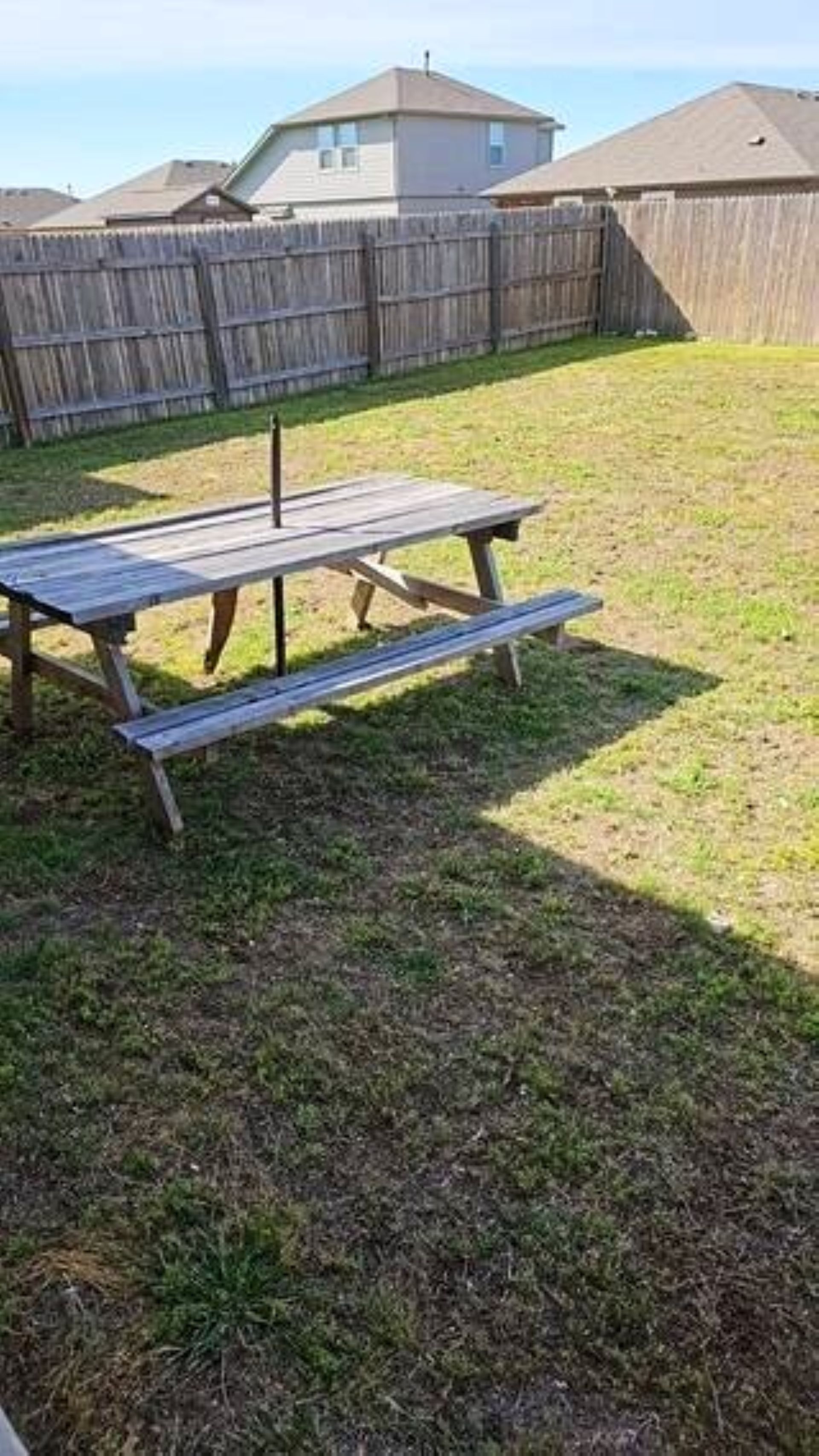 Une table de pique-nique en bois se trouve dans un jardin verdoyant, avec une clôture en bois en arrière-plan.