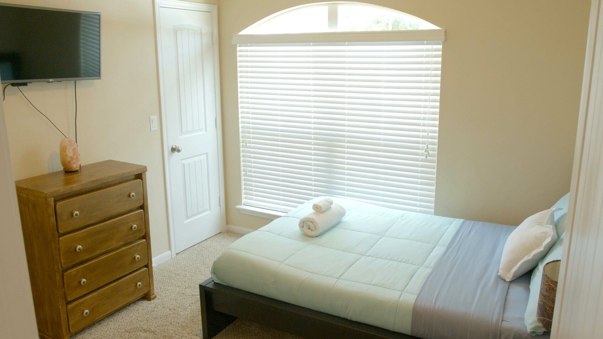 A bedroom with a bed, a dresser, a television, and a window with blinds.