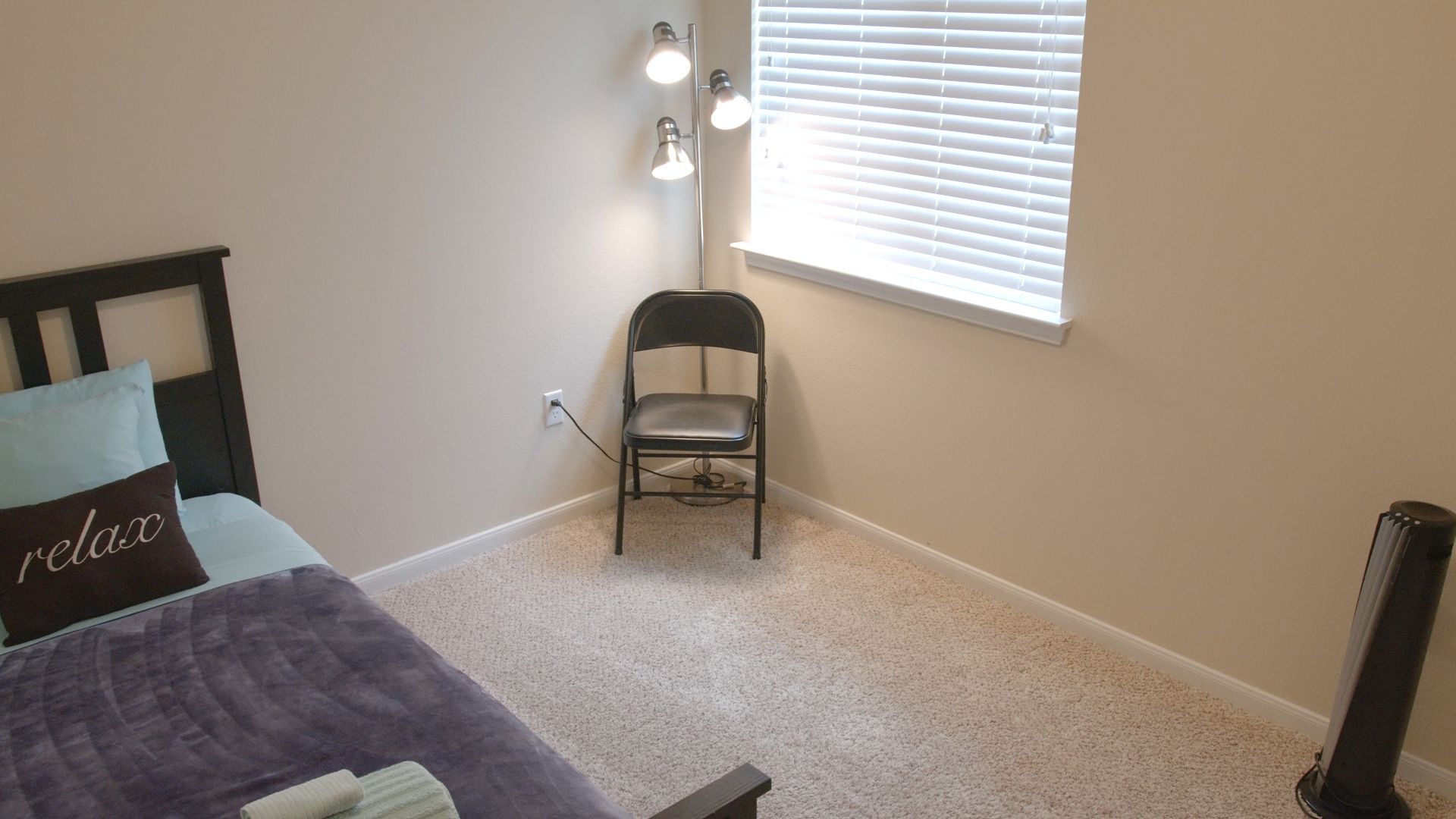 Ein Schlafzimmer mit einem Bett, einem Sessel, einer Stehlampe und einem Fenster mit Jalousien.