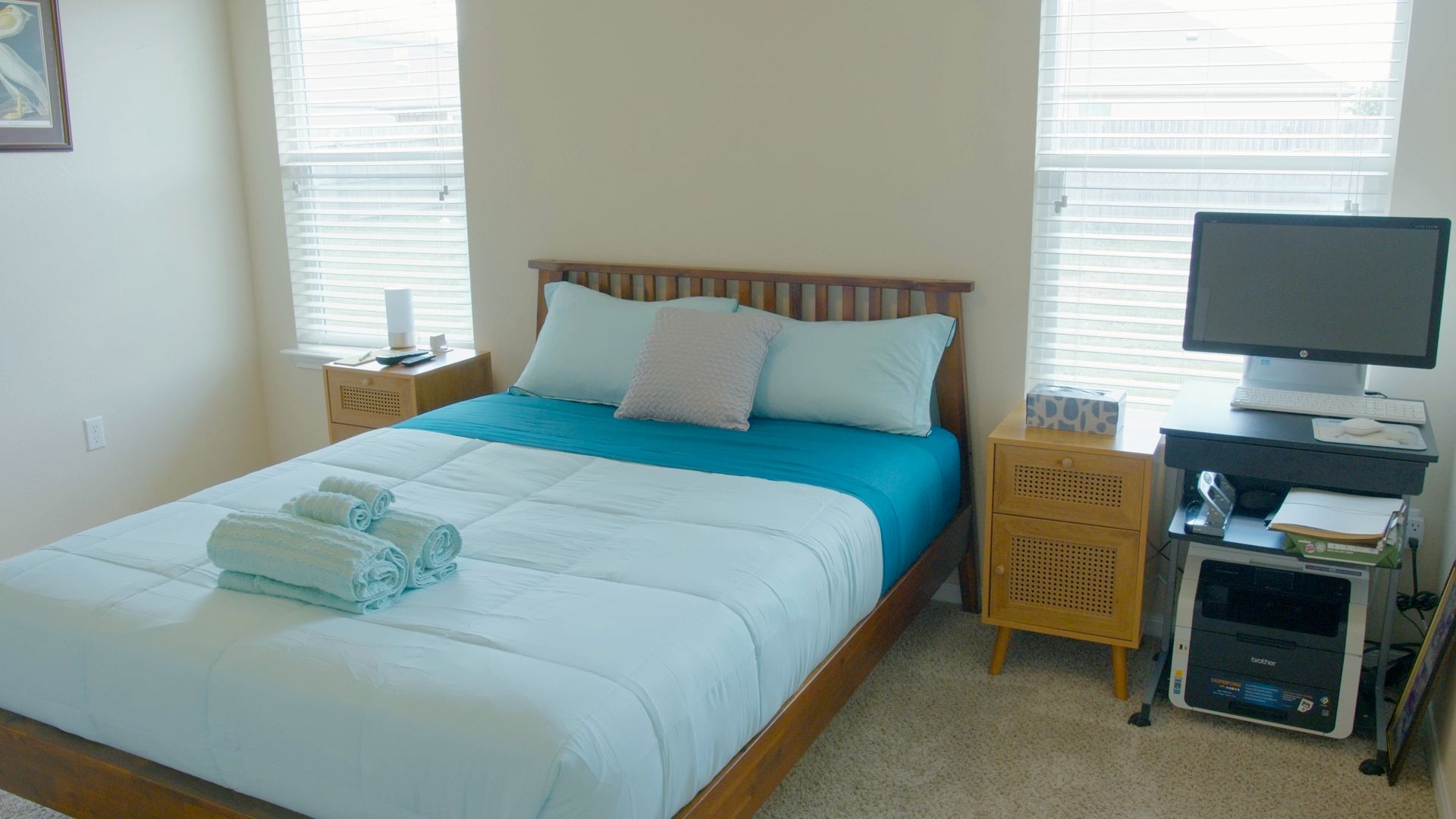 Een net opgemaakt bed met een blauw-witte dekbedovertrek, een houten hoofdbord en een nachtkastje met een lamp.