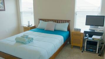 Een net opgemaakt bed met een blauw-witte dekbedovertrek, een houten hoofdbord en een nachtkastje met een lamp.