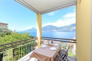 En balkon med et bord dækket til to, der giver udsigt over et naturskønt hav- og bjerglandskab.