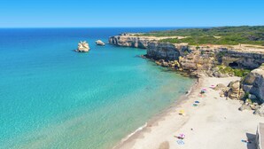 A beach with clear turquoise waters, rocky cliffs, and a sandy shore with umbrellas. - 3922 Villino Gioiellino by Barbarhouse (Melendugno)