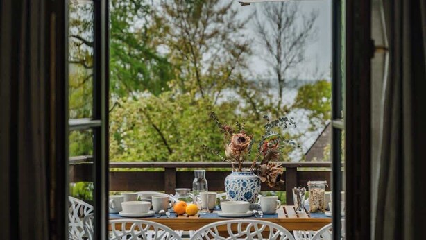 A view from a window with a table set for dining, featuring a vase with dried flowers and a bowl.