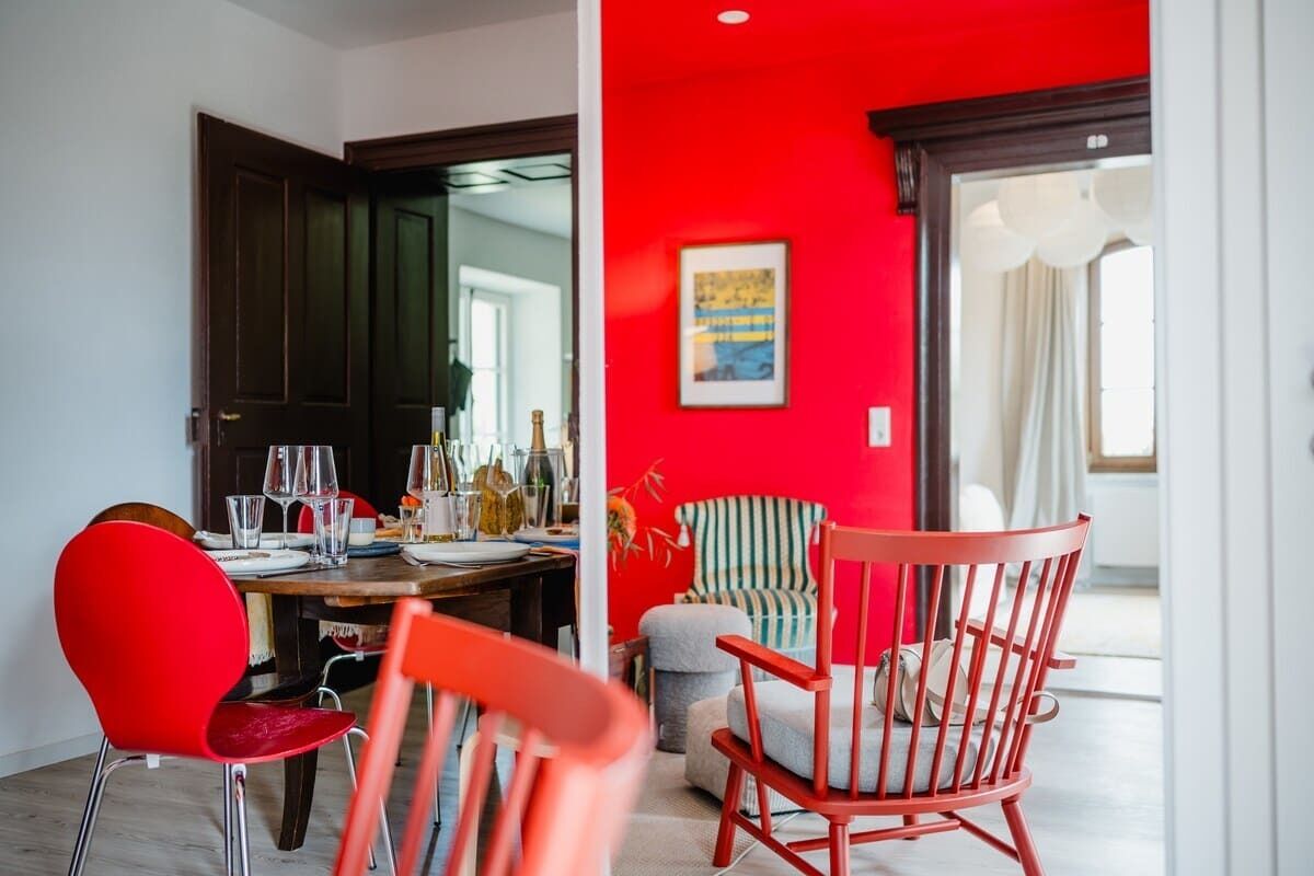 Un coin repas avec un mur rouge, une table à manger dressée avec des verres et des assiettes, et des chaises rouges.