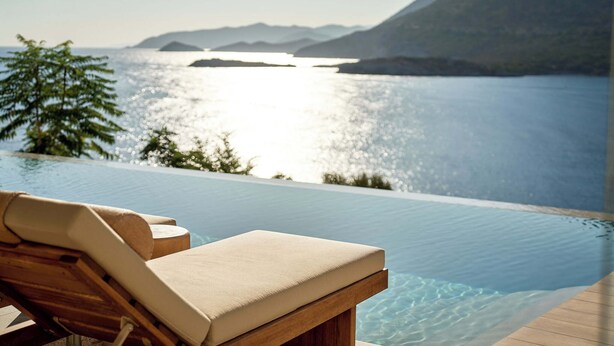 An infinity pool with a wooden deck and lounge chairs, overlooking a calm body of water and distant mountains. - Ficus Seafront Villa, Eco Pool & Close to Beach (CQ6M+WCC Bali, Greece)