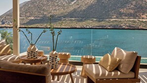 A balcony with a view of a mountain and a body of water. There is a sofa, a small round table, and a vase with decorative elements. - Ficus Seafront Villa, Eco Pool & Close to Beach (CQ6M+WCC Bali, Greece)