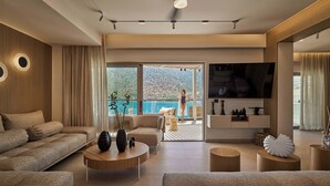 A modern living room with a sofa, armchairs, a coffee table, and a TV. There is a balcony with a view of the city. - Ficus Seafront Villa, Eco Pool & Close to Beach (CQ6M+WCC Bali, Greece)