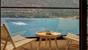 A balcony with wicker chairs, a small round table with a bowl, and a view of a coastal landscape with mountains and a body of water. - Ficus Seafront Villa, Eco Pool & Close to Beach (CQ6M+WCC Bali, Greece)