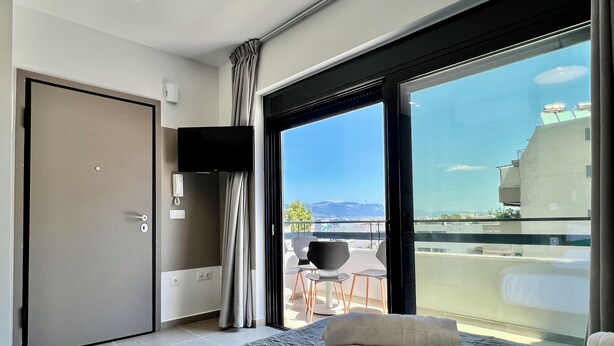 Une chambre d’hôtel moderne dotée d’un grand lit, d’une télévision à écran plat, d’un balcon offrant une vue sur la ville et les montagnes, et d’une porte coulissante.