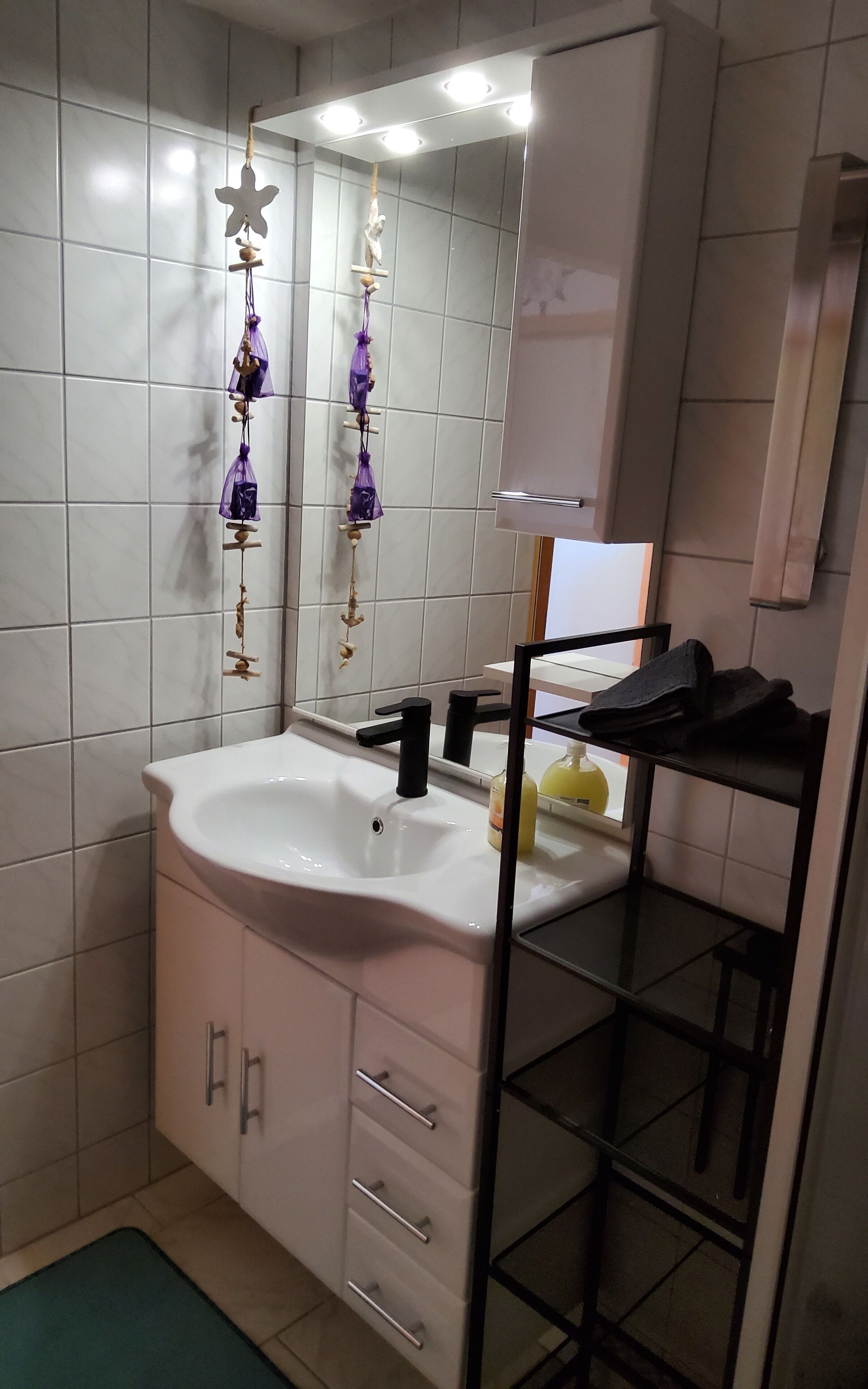 A bathroom with a white sink, black faucet, and a mirror above it. There are two purple hanging decorations and a yellow bottle on the sink.